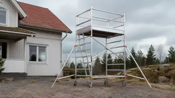Mobil byggställning med låsta hjul, stödben, plattform, räcken och fotlist vid ett hus